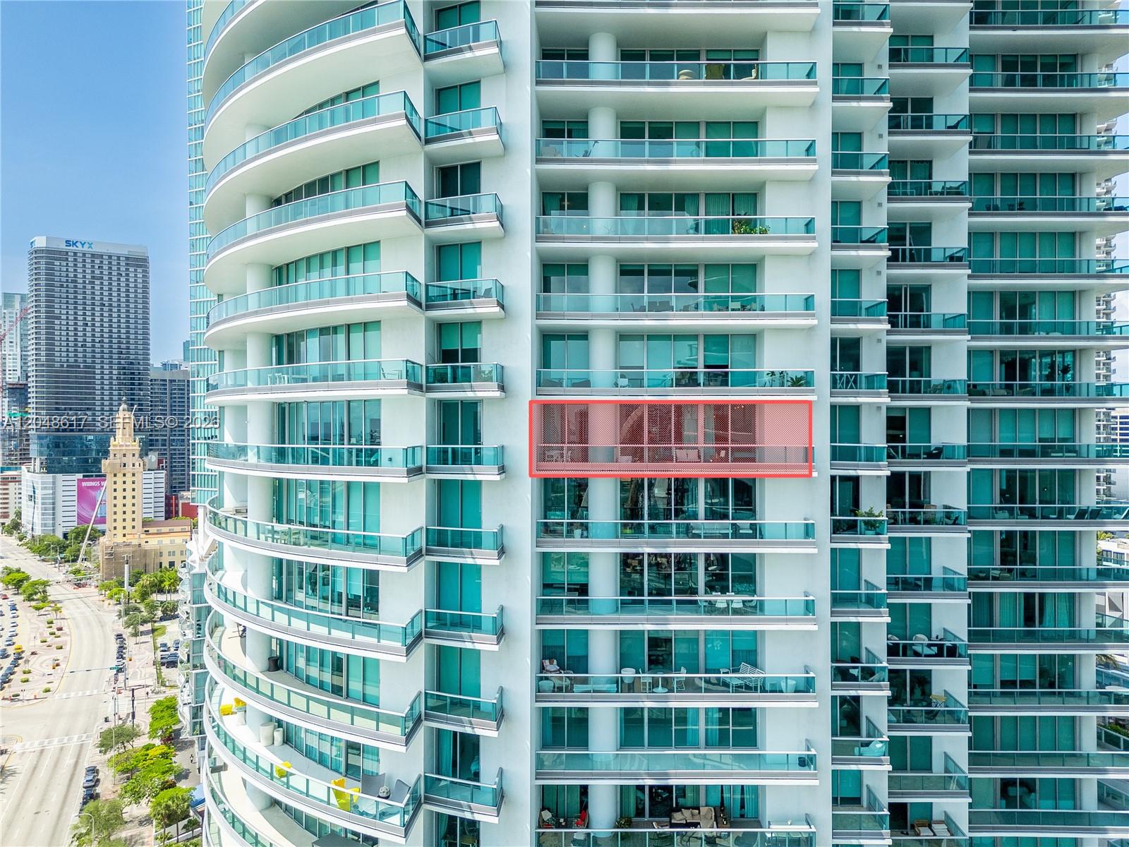 An exterior view of a high-rise building featuring a highlighted balcony with glass railings — 900 Biscayne Blvd # 2408, Miami FL 33132, MIAMI, FL