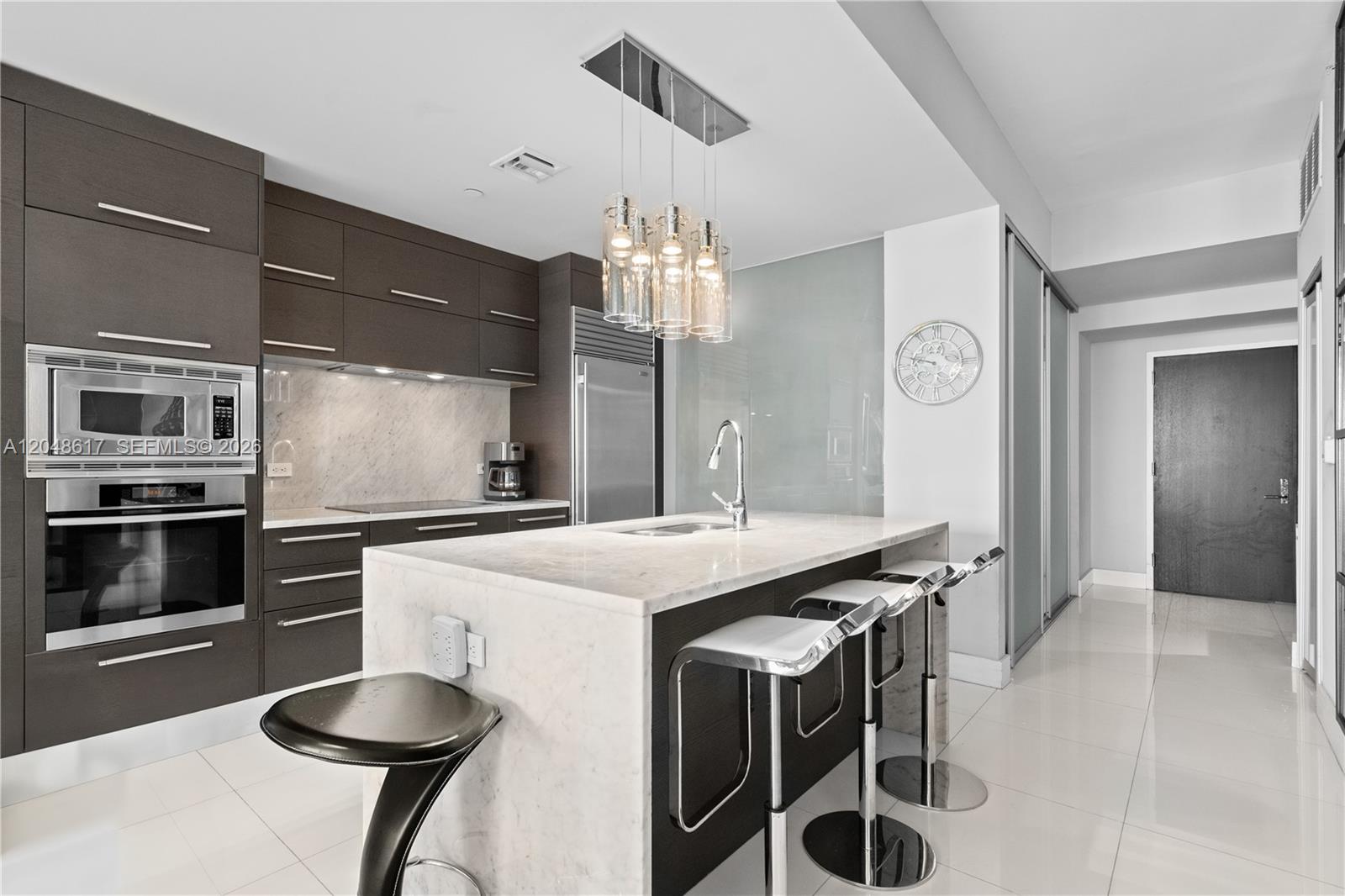 A modern kitchen features dark wood cabinetry, a marble-topped island, and stainless steel appliances — 900 Biscayne Blvd # 2408, Miami FL 33132, MIAMI, FL