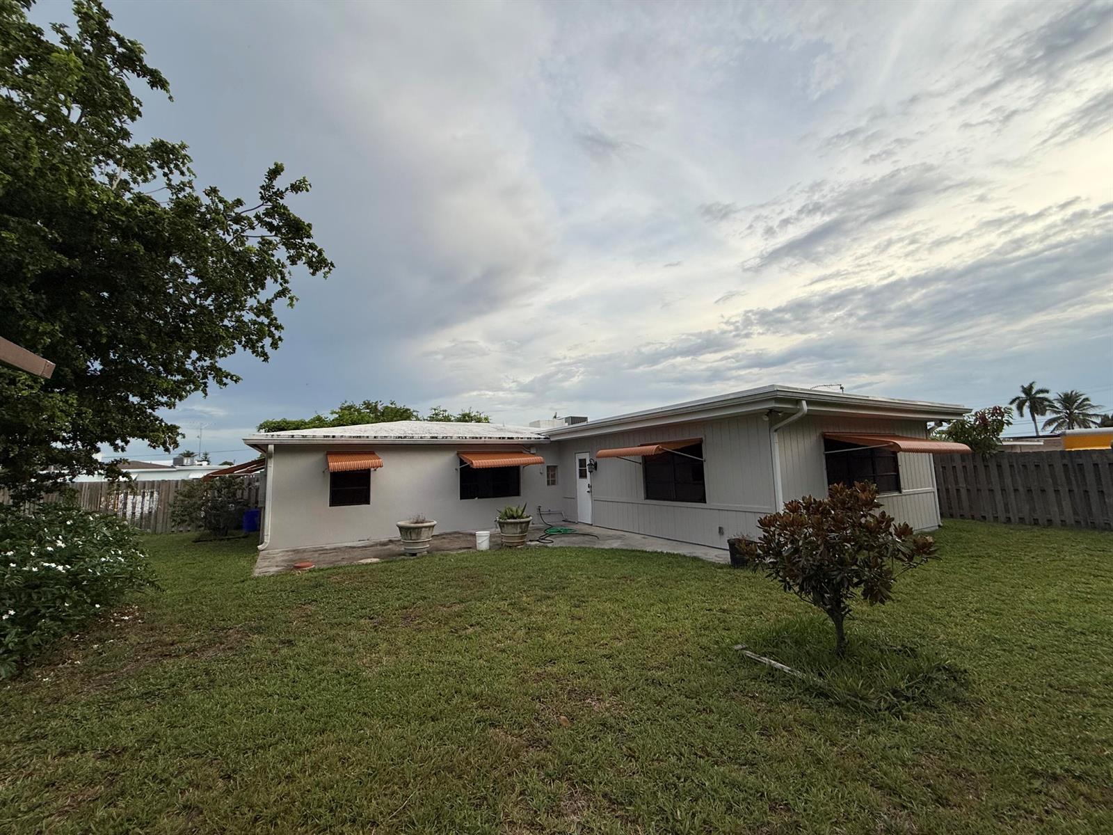 The exterior of a single-story house features light-colored siding, orange awnings, and a grassy yard — 817 Elm Road, West Palm Beach FL 33409, WEST PALM BEACH, FL