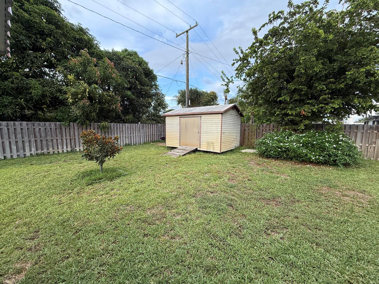 A backyard features a small storage shed, a wooden fence, and mature trees — 817 Elm Road, West Palm Beach FL 33409, WEST PALM BEACH, FL