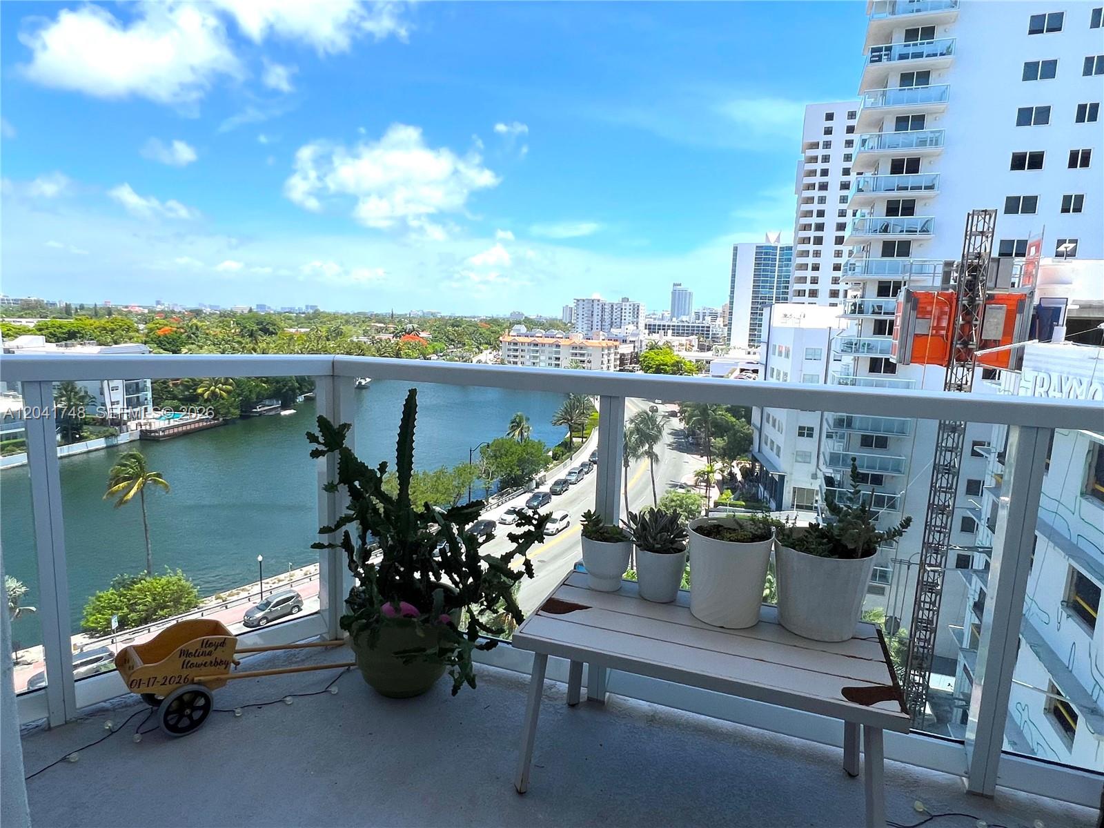 A balcony view overlooking a waterway, a road, and nearby high-rise buildings — 2401 Collins Ave # 1009, Miami Beach FL 33140, MIAMI BEACH, FL