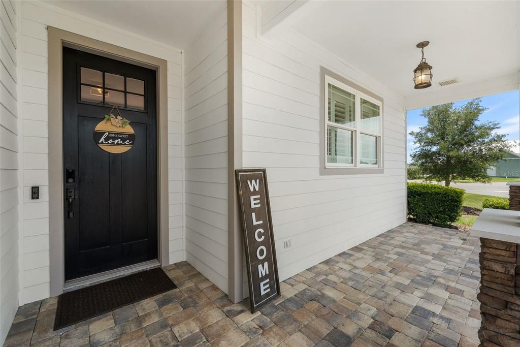 A front porch features a black door, a welcome sign, and stone-look paver flooring — 24674 SW 19TH PLACE, NEWBERRY, FL