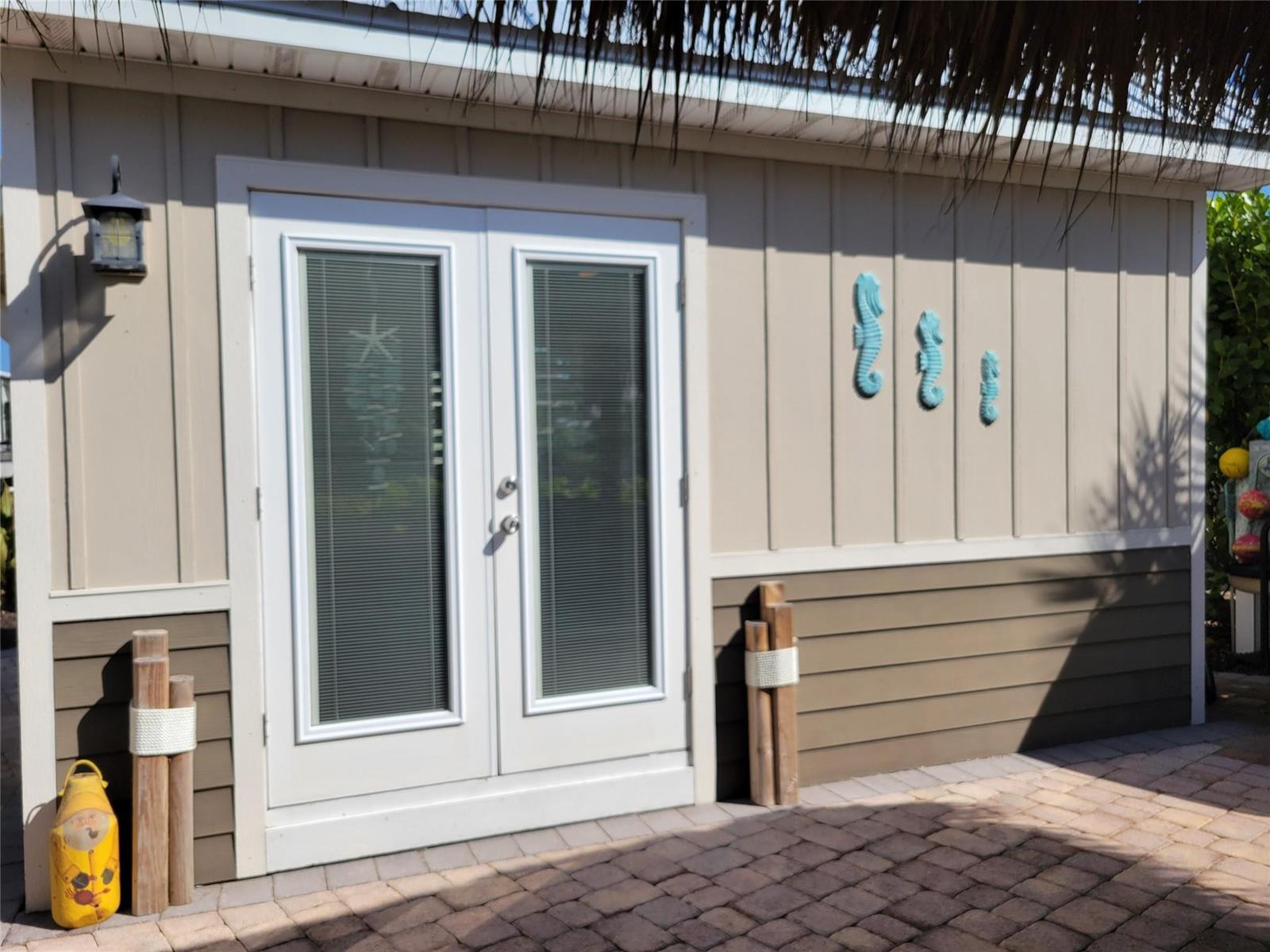 A beige exterior wall features double glass doors, seahorse wall decor, and a brick patio — 628 SW 35th, Okeechobee FL 34974, OKEECHOBEE, FL