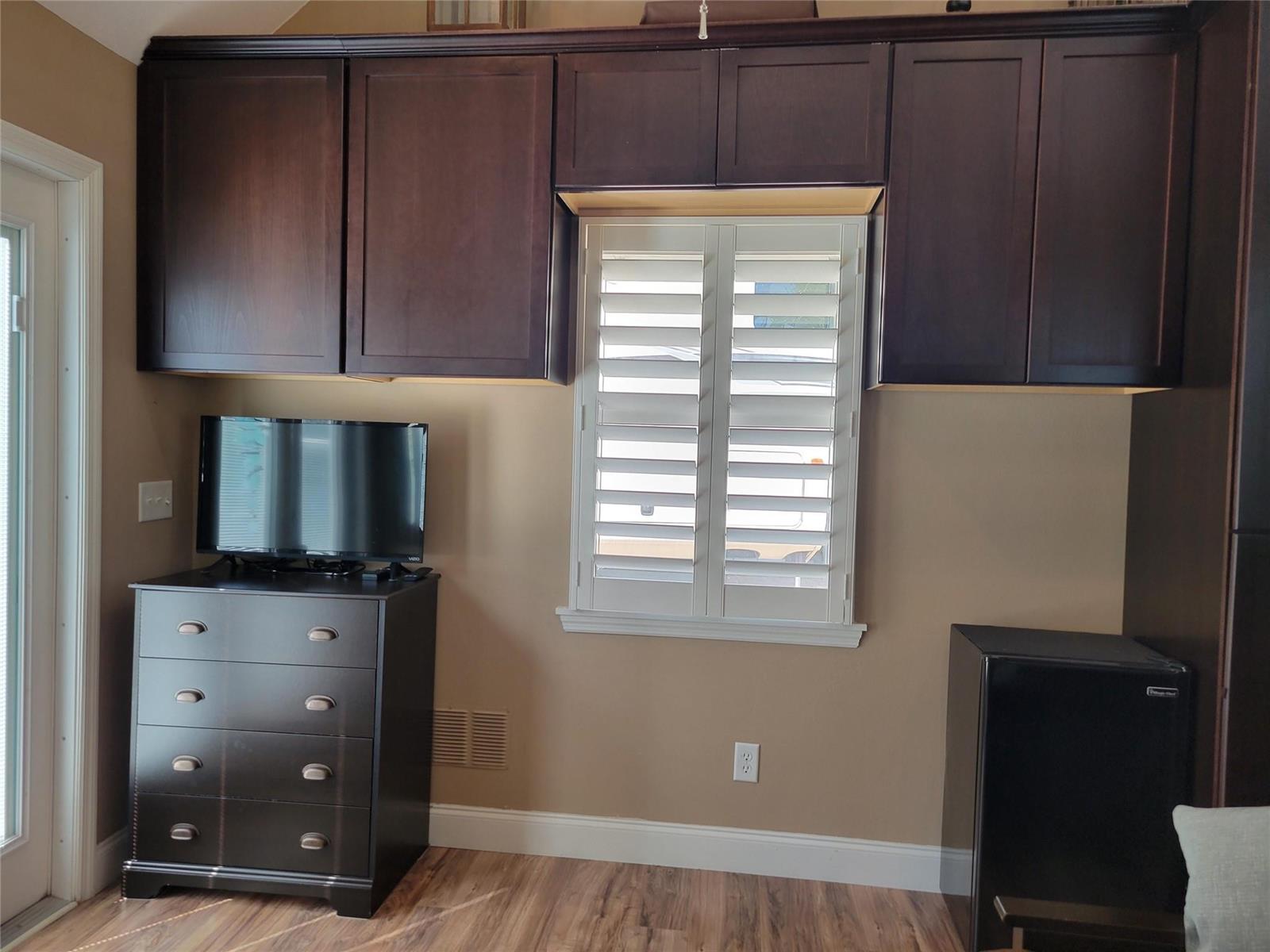 A room features dark wood cabinetry above a window, a dresser with a television, and a refrigerator — 628 SW 35th, Okeechobee FL 34974, OKEECHOBEE, FL