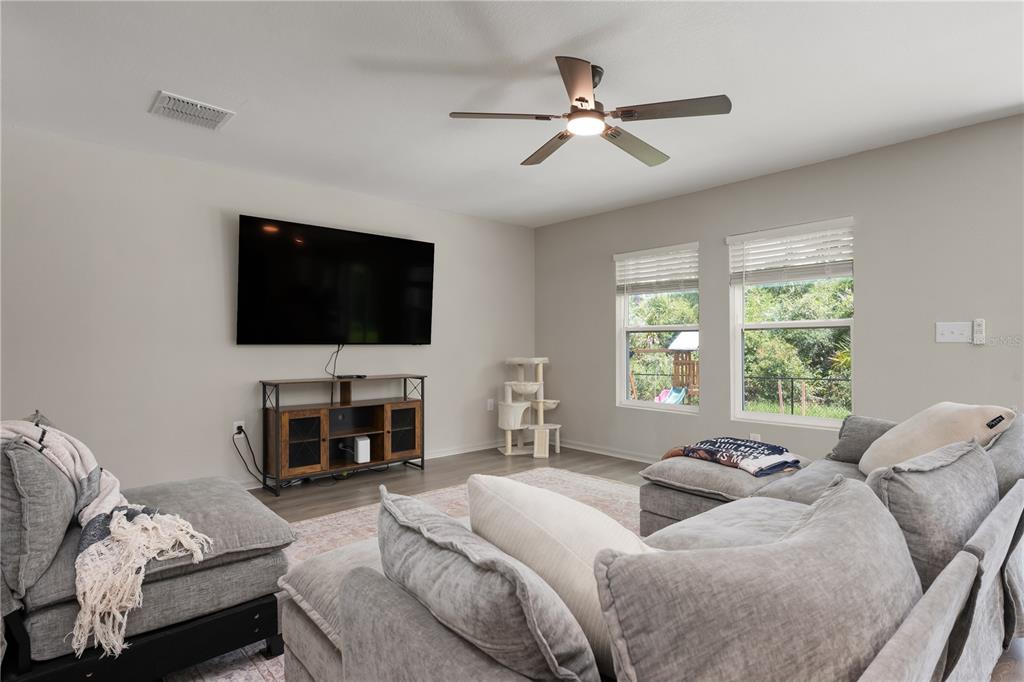 A living room features a large sectional sofa, a wall-mounted television, and two windows — 15530 MAYNARD AVENUE, PORT CHARLOTTE, FL