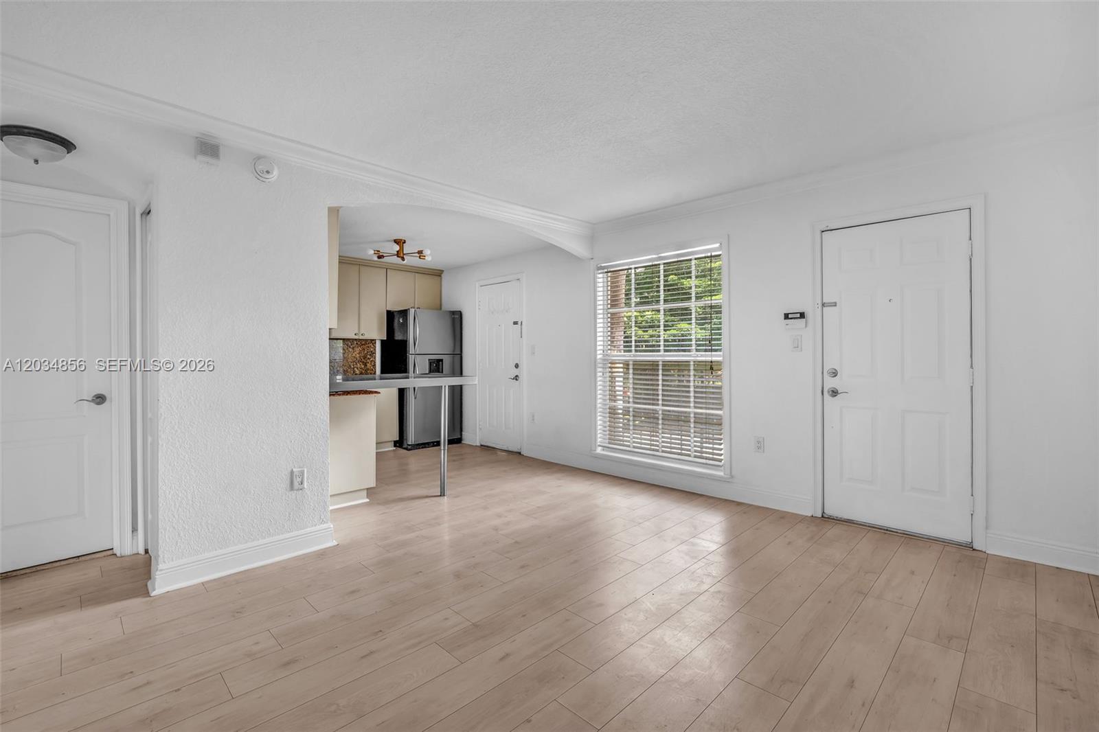 This room features light wood-look flooring, white walls, a window, and an adjacent kitchen area — 3245 Virginia St # 24, Miami FL 33133, MIAMI, FL