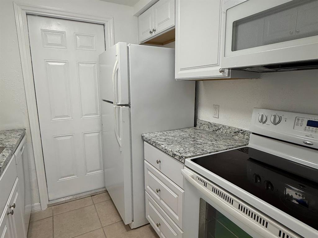 A kitchen features white cabinets, granite countertops, and white appliances including a refrigerator and stove — 4954 BITNER STREET, NEW PORT RICHEY, FL