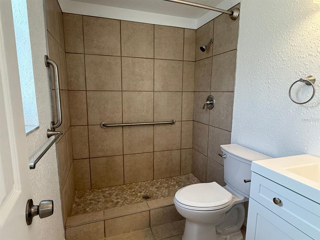A bathroom features a tiled walk-in shower with grab bars and a white vanity — 4954 BITNER STREET, NEW PORT RICHEY, FL