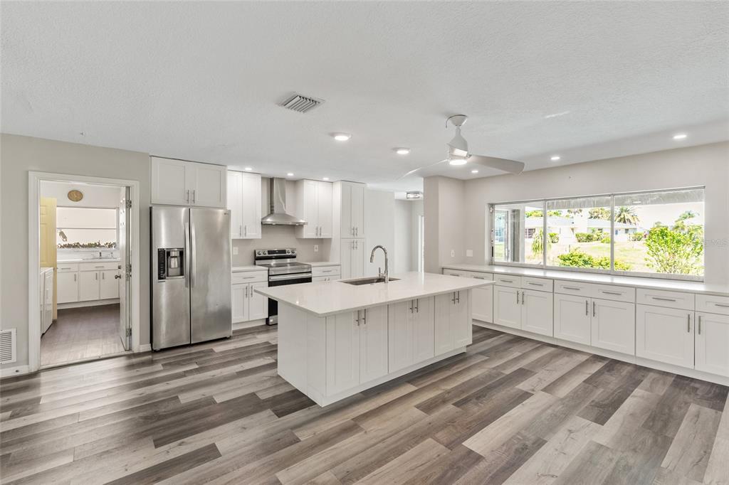 A modern kitchen features white cabinetry, a large center island, and wood-look flooring — 1009 KINGS COURT, VENICE, FL