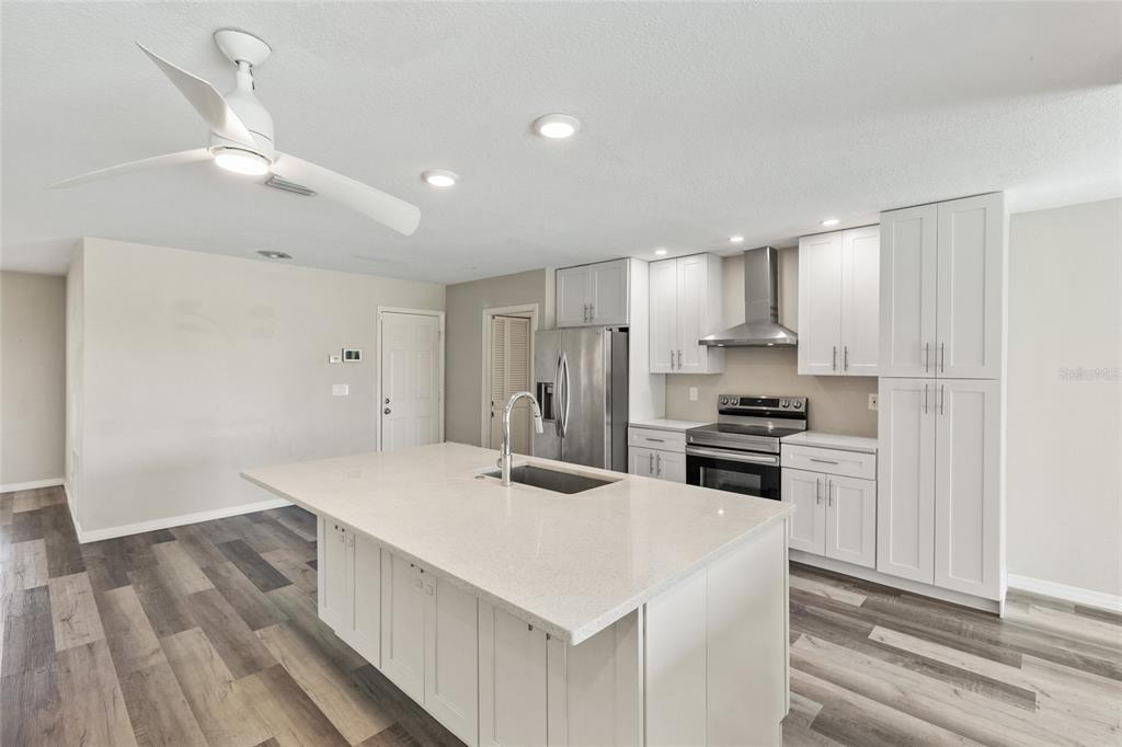 A modern kitchen features white cabinetry, a large quartz island, and wood-look flooring — 1009 KINGS COURT, VENICE, FL