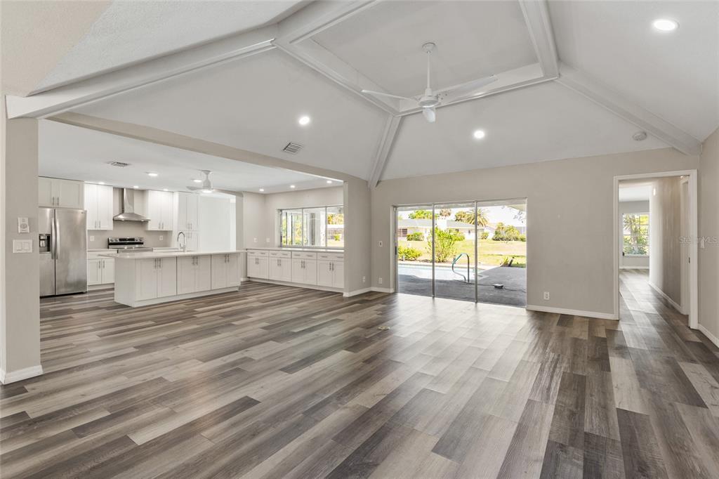 An open-concept living area with vaulted ceilings, white kitchen cabinetry, and wood-look flooring — 1009 KINGS COURT, VENICE, FL