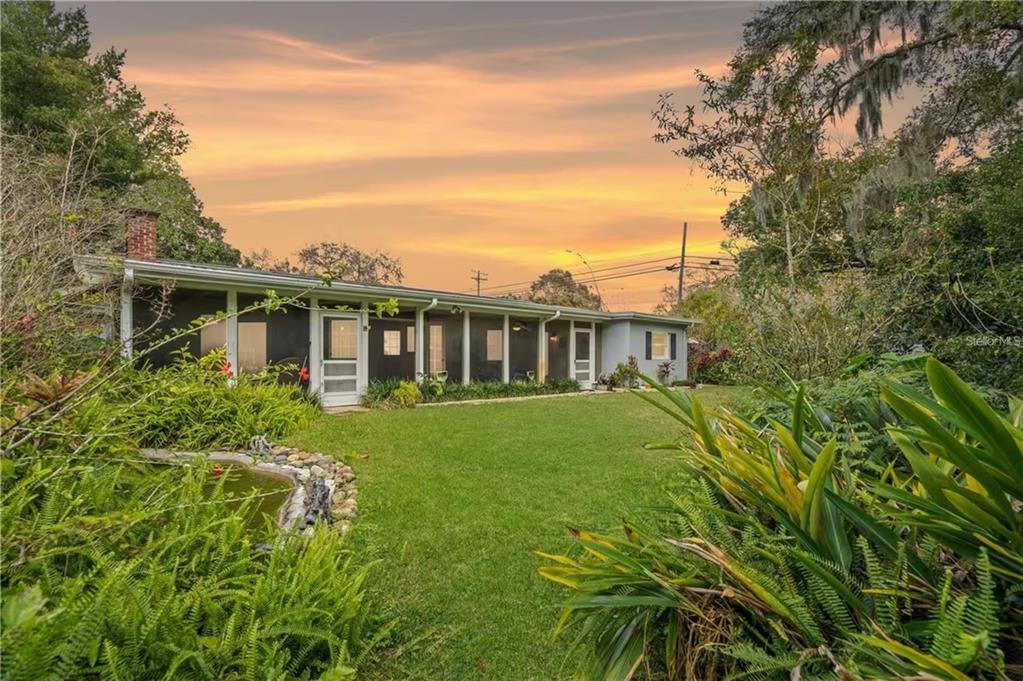A single-story house with a screened-in porch sits behind a grassy lawn and pond — 2102 W KYRA DRIVE, TAMPA, FL