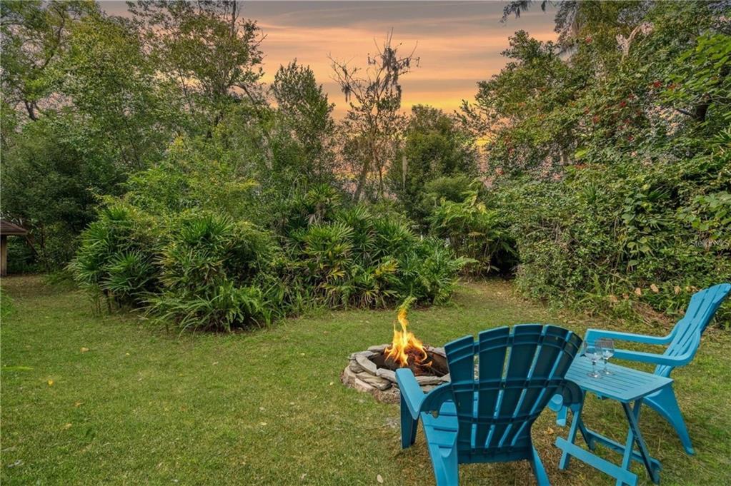 A backyard fire pit area features two blue chairs on a grassy lawn at sunset — 2102 W KYRA DRIVE, TAMPA, FL