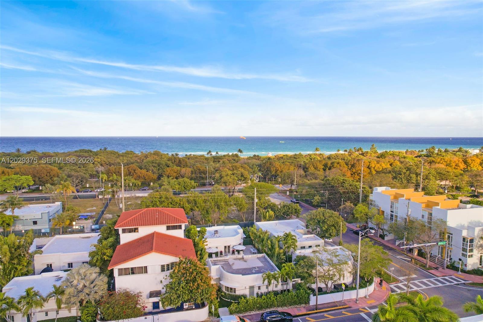 An aerial view shows a coastal neighborhood with houses, lush trees, and the ocean beyond — 8109 Harding Ave, Miami Beach FL 33141, MIAMI BEACH, FL