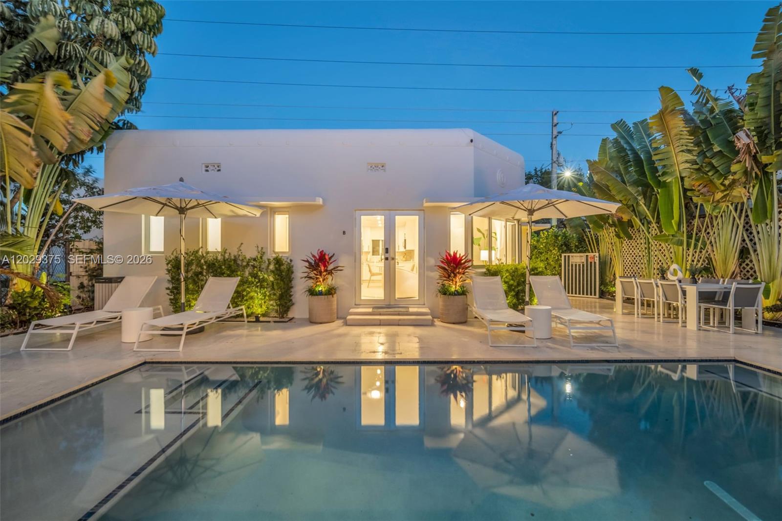 A white house exterior with a swimming pool, lounge chairs, and umbrellas at dusk — 8109 Harding Ave, Miami Beach FL 33141, MIAMI BEACH, FL