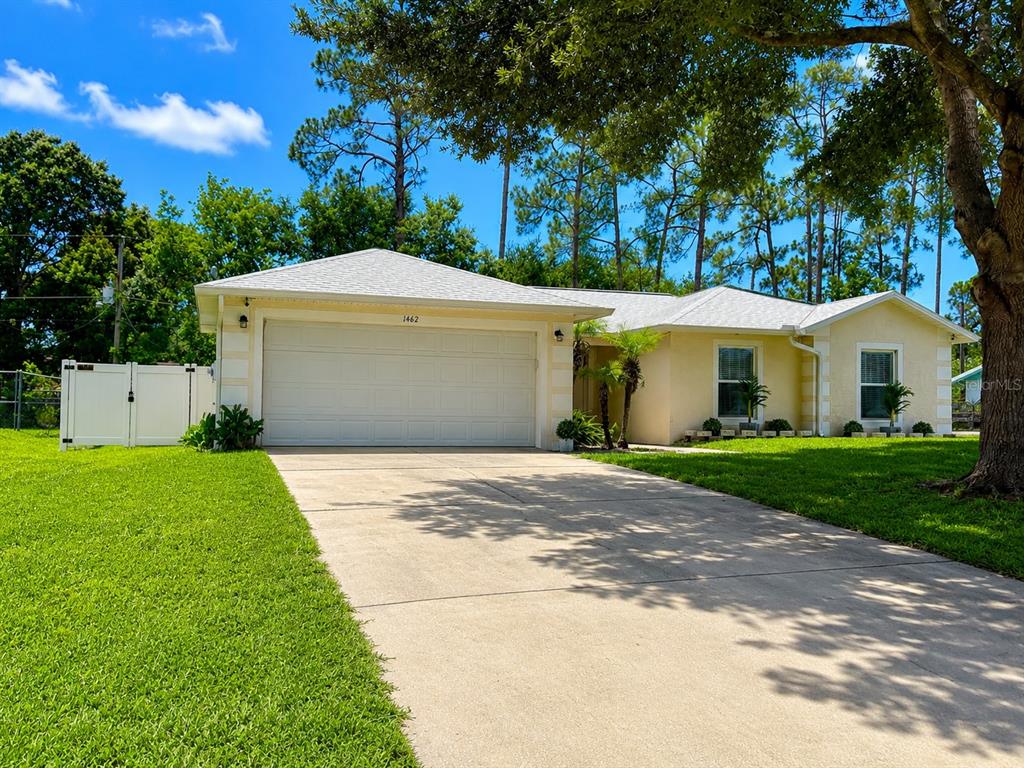 A single-story house with a white garage door, light yellow siding, and a concrete driveway — 1462 ADMIRAL NIMITZ AVE, DAYTONA BEACH, FL