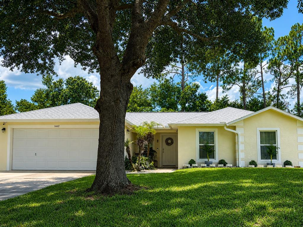 A single-story yellow house with a two-car garage and a large tree in front — 1462 ADMIRAL NIMITZ AVE, DAYTONA BEACH, FL