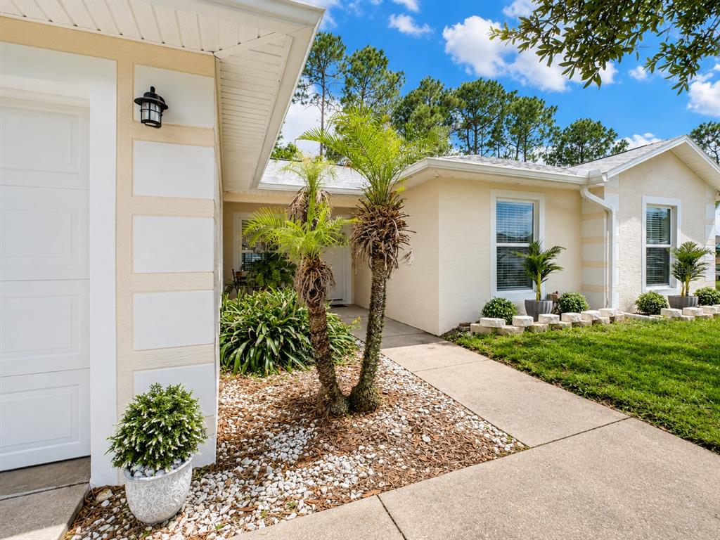 A beige house exterior features a white garage door, palm trees, and a concrete walkway — 1462 ADMIRAL NIMITZ AVE, DAYTONA BEACH, FL