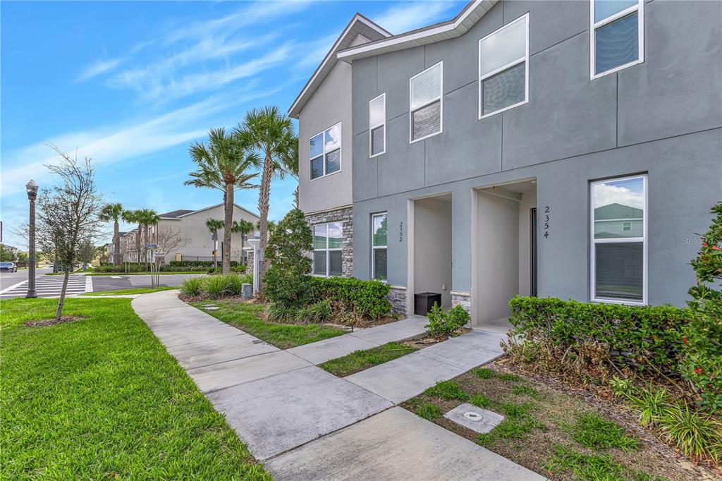 A two-story gray townhouse exterior features a concrete walkway, landscaping, and two separate entryways — 2354 ZABALLINA PLACE, KISSIMMEE, FL