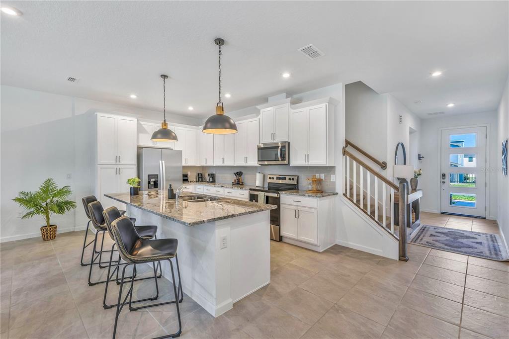 A kitchen with white cabinets, granite countertops, a center island with stools, and tile flooring — 2354 ZABALLINA PLACE, KISSIMMEE, FL
