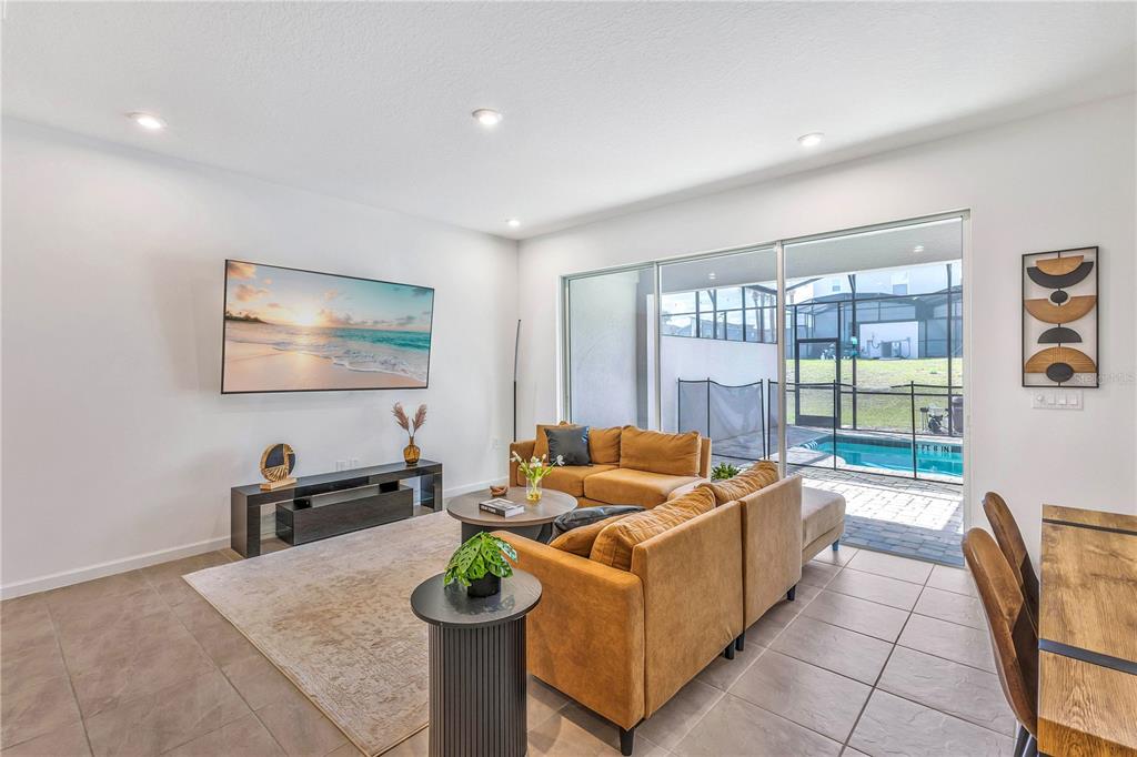 A living room features a wall-mounted television, mustard-colored sectional sofa, and sliding doors to a pool — 2354 ZABALLINA PLACE, KISSIMMEE, FL