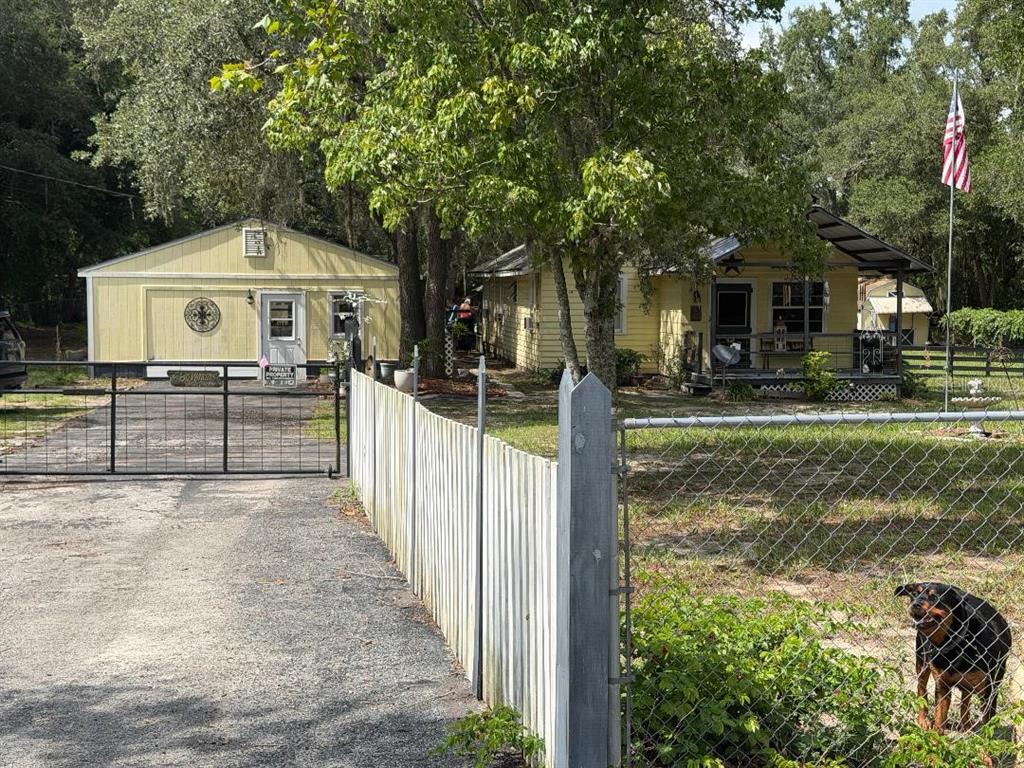 A yellow house and detached garage are visible behind a fenced yard with a dog — 11705 MARY LOU DRIVE, HUDSON, FL