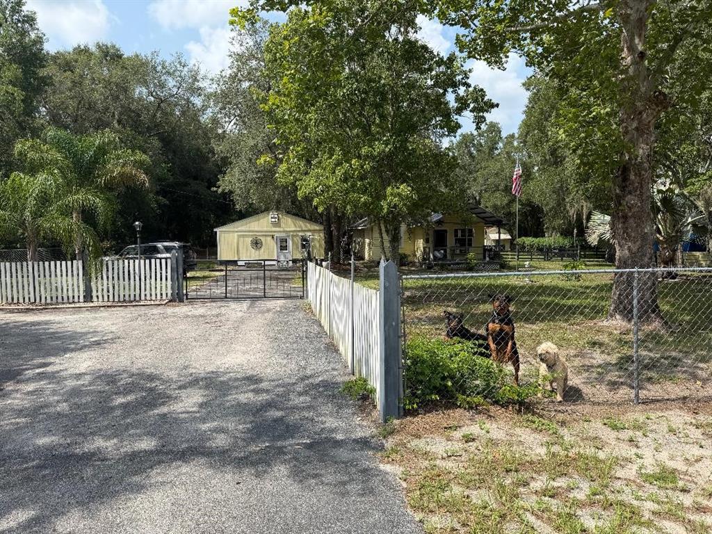 A gravel driveway leads to a yellow house and detached garage behind a fenced yard — 11705 MARY LOU DRIVE, HUDSON, FL