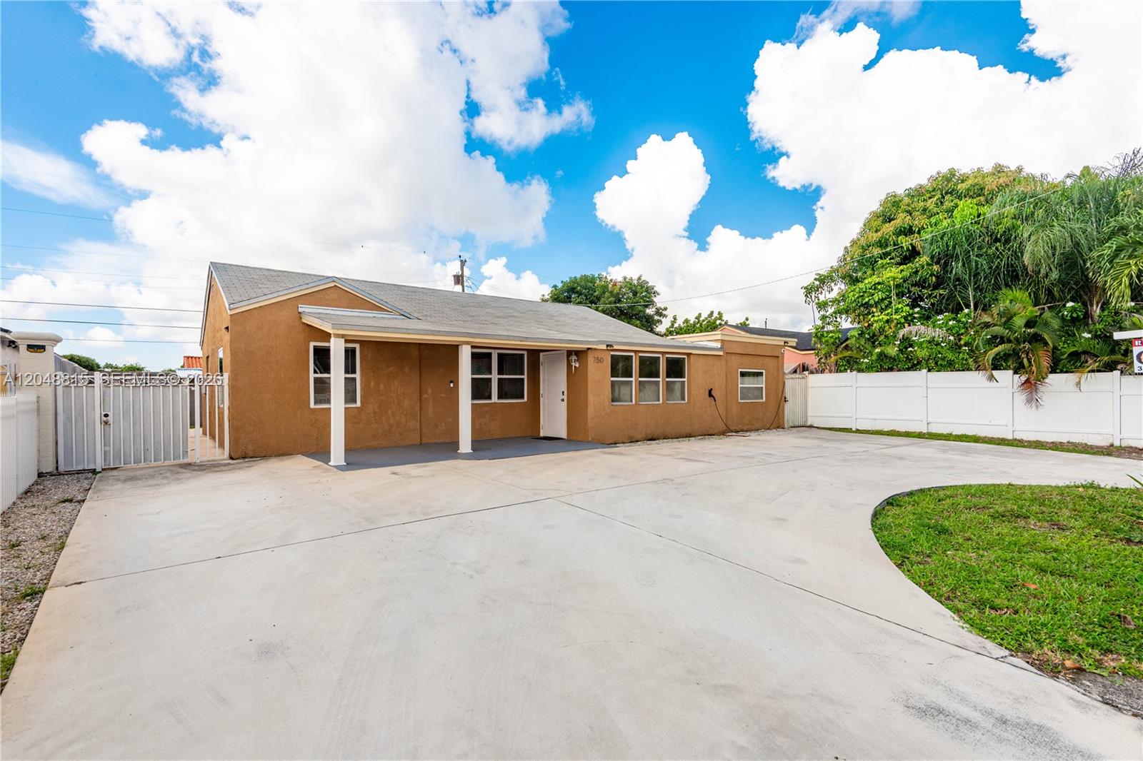 A single-story tan house with a concrete driveway and a white fence — 750 NE 4th Pl, Hialeah FL 33010, HIALEAH, FL
