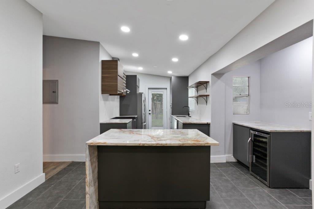 A modern kitchen features a marble-topped island, dark gray cabinetry, and a wine refrigerator — 3417 SE TENNESSEE TERRACE, ORLANDO, FL