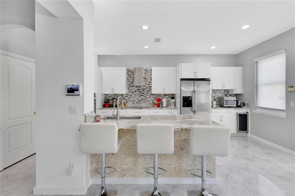 A modern kitchen features white cabinetry, a marble-topped island with three stools, and tile flooring — 4730 CAPITAL BOULEVARD, ST CLOUD, FL