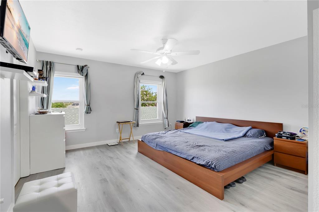 A bedroom features light gray wood-look flooring, a wooden bed frame, and two windows — 4730 CAPITAL BOULEVARD, ST CLOUD, FL