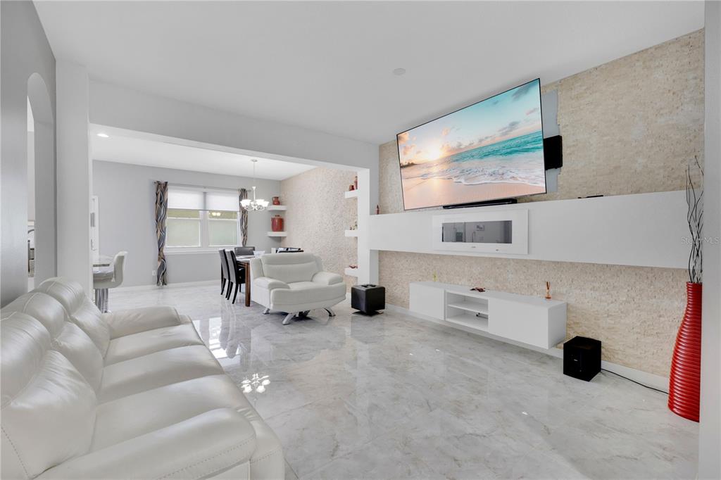 A living room with white leather furniture, a wall-mounted television, and light stone wall accents — 4730 CAPITAL BOULEVARD, ST CLOUD, FL