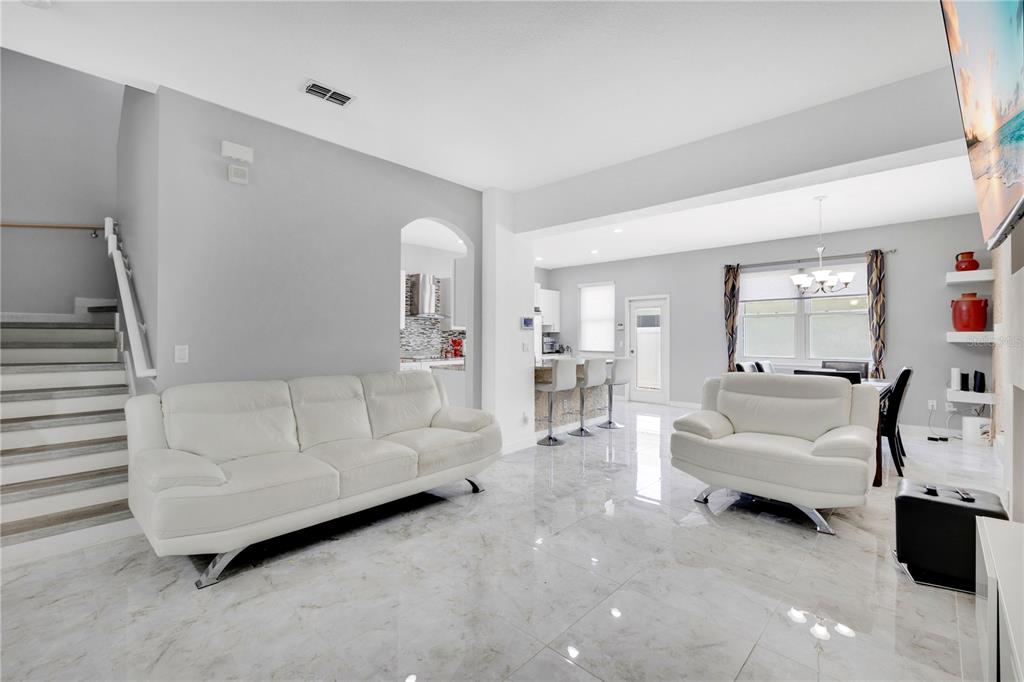A living room with white leather furniture, marble-look tile flooring, and an adjacent kitchen area — 4730 CAPITAL BOULEVARD, ST CLOUD, FL