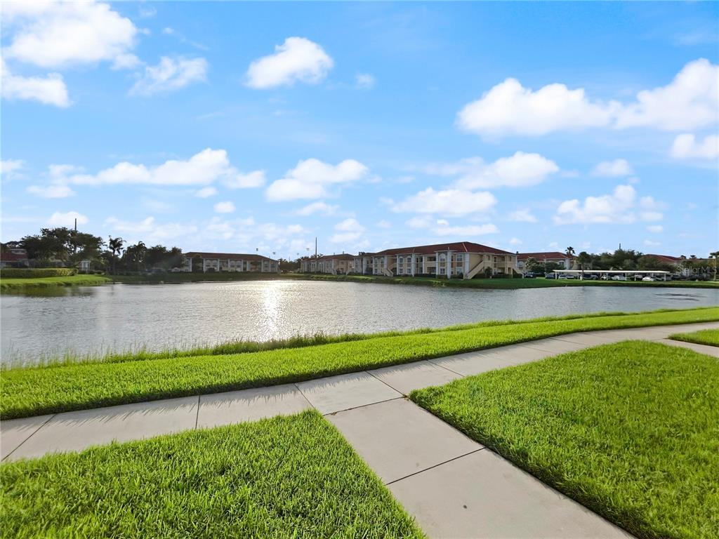 A concrete walkway leads through a grassy lawn toward a lake and apartment buildings — 1025 VILLAGIO CIRCLE UNIT 101, SARASOTA, FL