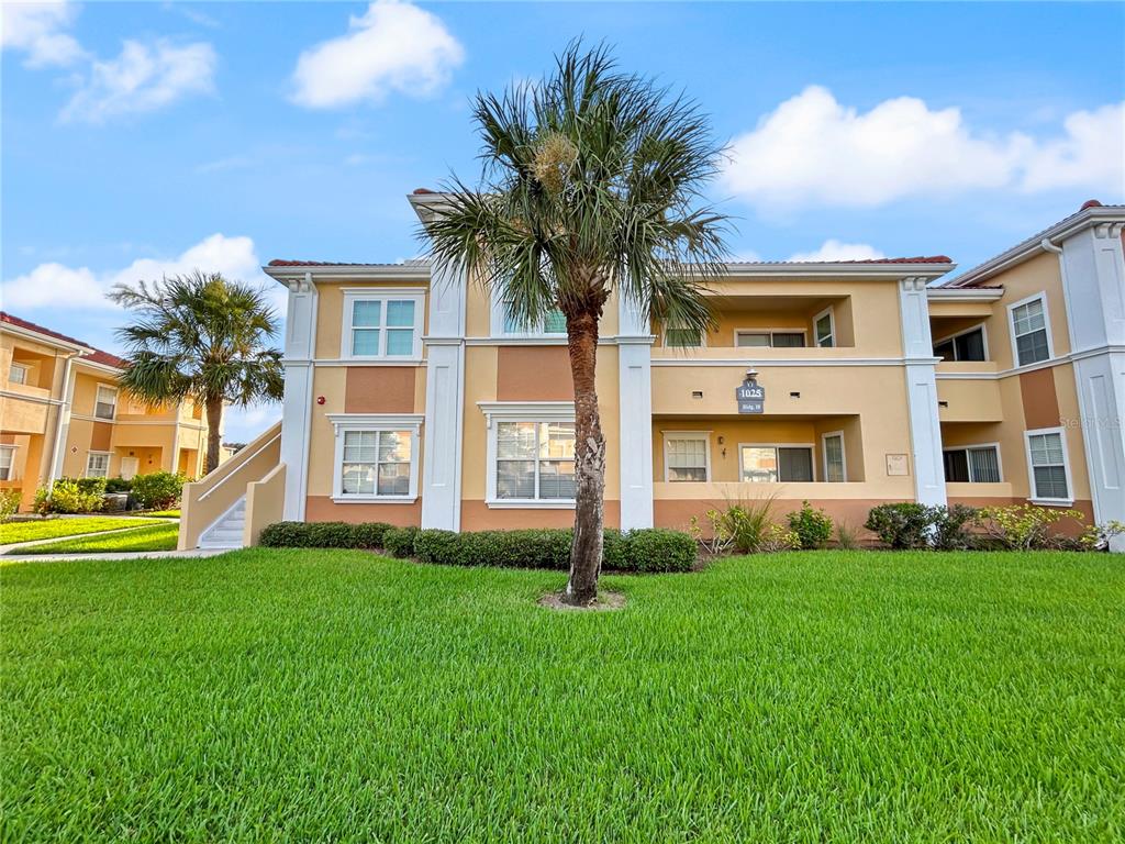 A three-story apartment building with tan stucco walls and a palm tree in the foreground — 1025 VILLAGIO CIRCLE UNIT 101, SARASOTA, FL