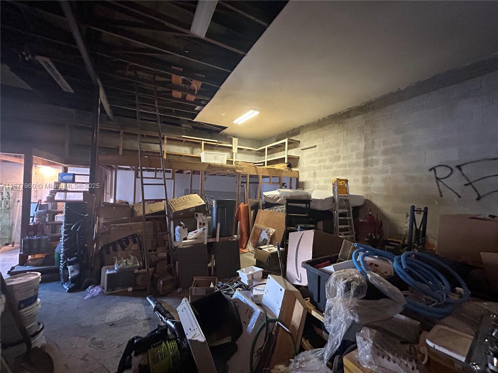 A cluttered, unfinished storage room features exposed ceiling joists, concrete block walls, and shelving — 2028 Buchanan St, Hollywood FL 33020, HOLLYWOOD, FL