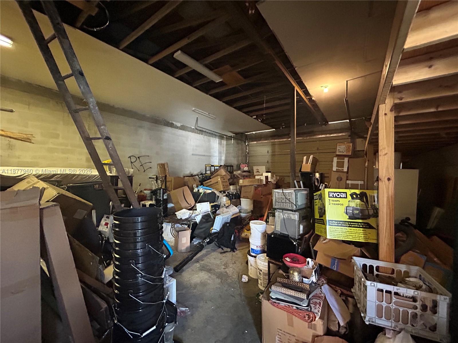 A cluttered garage with exposed ceiling joists, concrete block walls, and various stored items — 2028 Buchanan St, Hollywood FL 33020, HOLLYWOOD, FL
