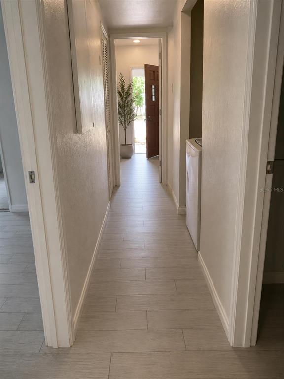 A hallway with light wood-look tile flooring leads to an open exterior door — 1838 COLTON DRIVE, ORLANDO, FL