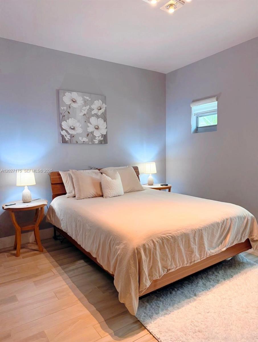 A bedroom features a wooden bed frame, light-colored bedding, two nightstands, and floral wall art — 2135 Washington Ct # 7, Miami Beach FL 33139, MIAMI BEACH, FL