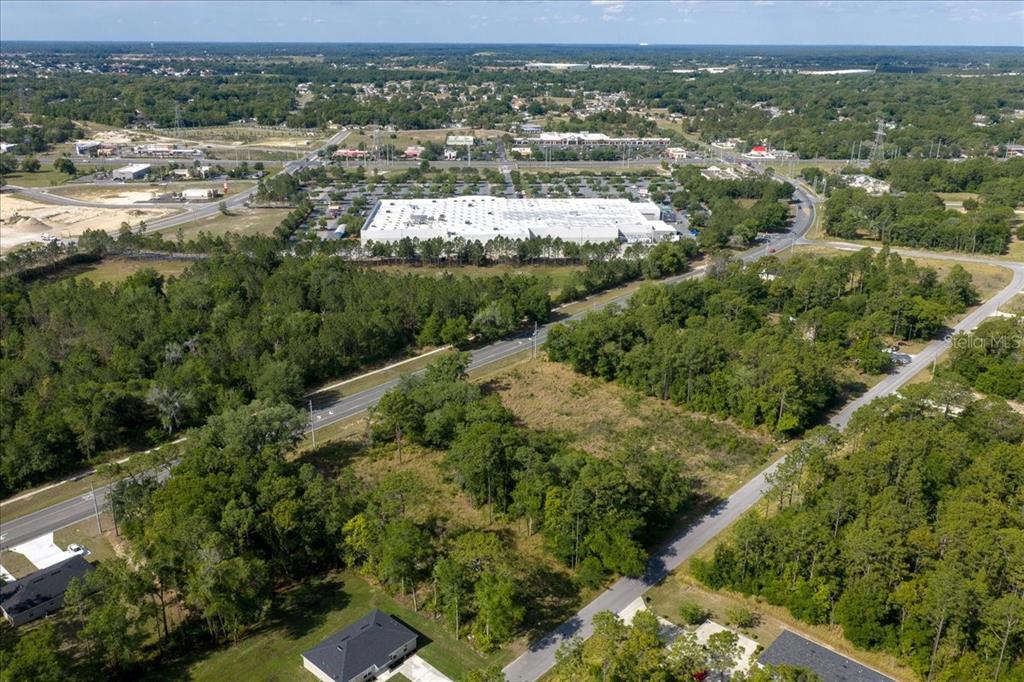 An aerial view shows a large, undeveloped wooded lot situated near a commercial shopping center — BAHIA TERRACE DRIVE, OCALA, FL