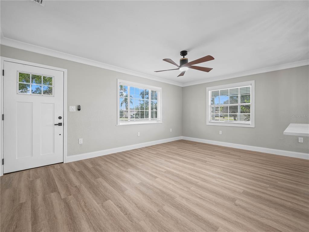 A bright, empty room features light wood-look flooring, gray walls, two windows, and a ceiling fan — 125 80TH AVENUE N, ST PETERSBURG, FL