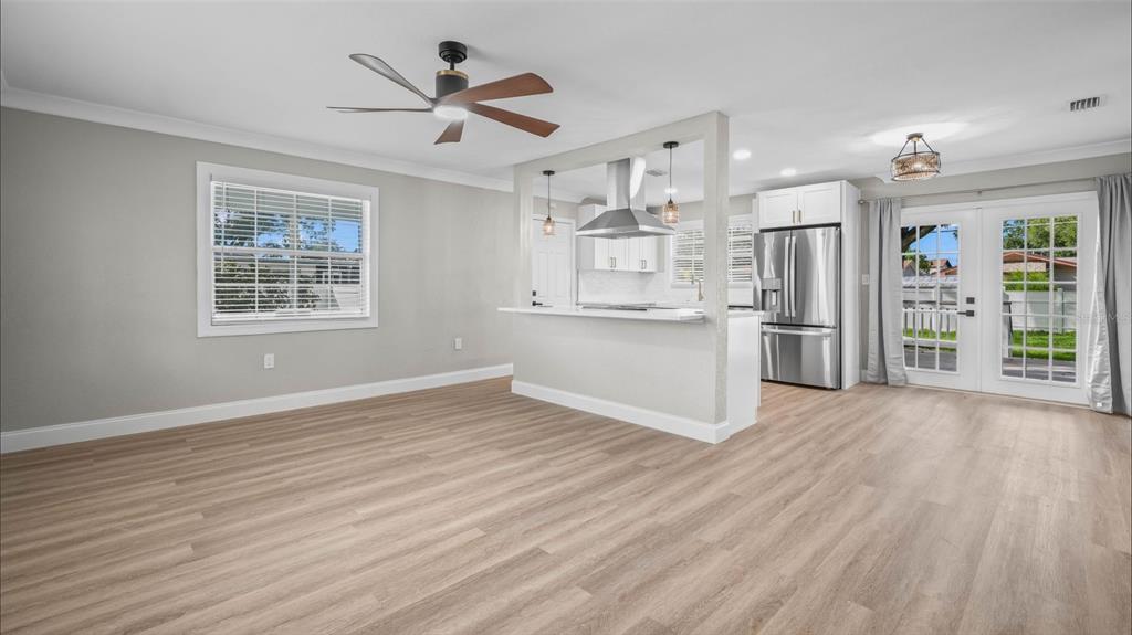 An open-concept living area features light wood-look flooring, a kitchen island, and French doors — 125 80TH AVENUE N, ST PETERSBURG, FL