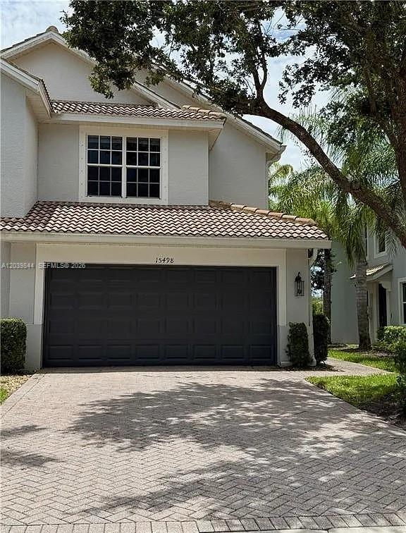 A two-story house features a dark garage door, a tiled roof, and a paved driveway — 15498 Marcello Cir, Naples FL 34110, NAPLES, FL
