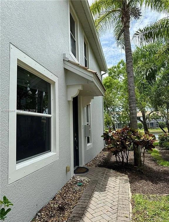 A side view of a light-colored house exterior featuring a window, doorway, and brick walkway — 15498 Marcello Cir, Naples FL 34110, NAPLES, FL