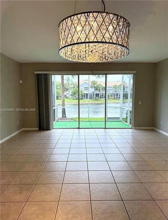 A tiled room features a large crystal drum chandelier and sliding doors overlooking a lake — 15498 Marcello Cir, Naples FL 34110, NAPLES, FL