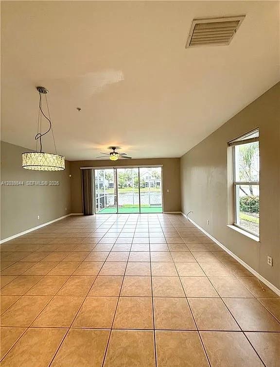 An empty living room features beige tile flooring, a modern chandelier, and sliding glass doors — 15498 Marcello Cir, Naples FL 34110, NAPLES, FL