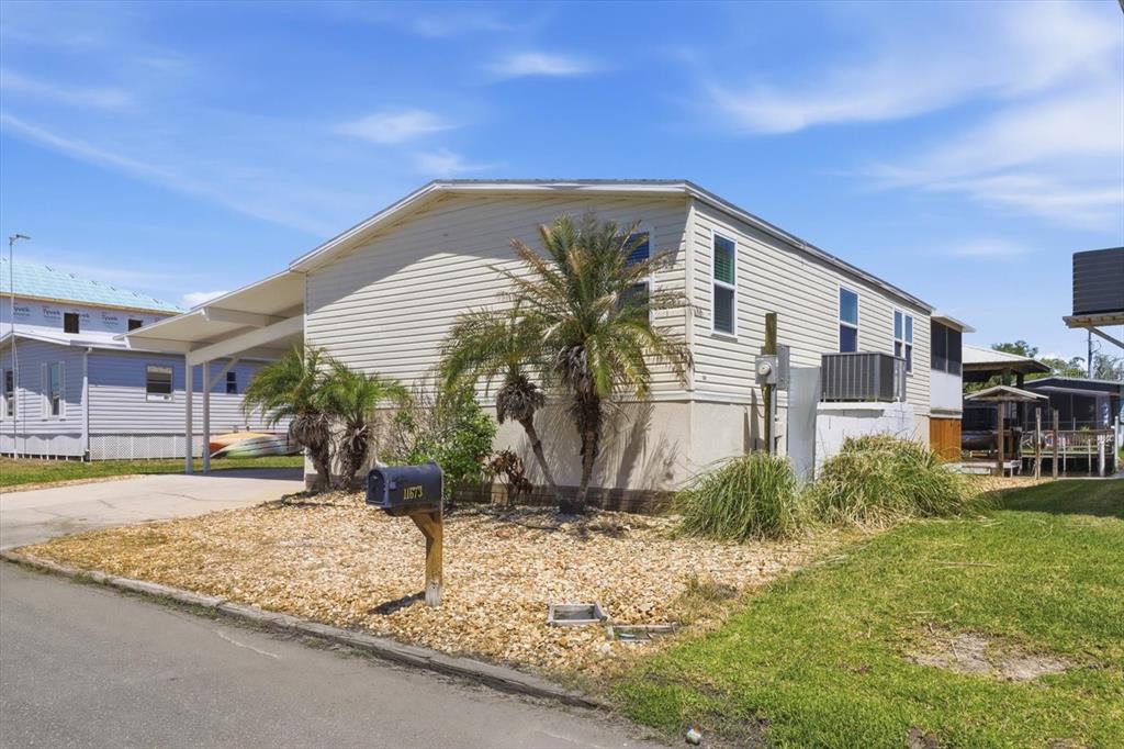 A single-story manufactured home with light siding, a carport, and a gravel front yard — 11673 W CLEARWATER COURT, HOMOSASSA, FL