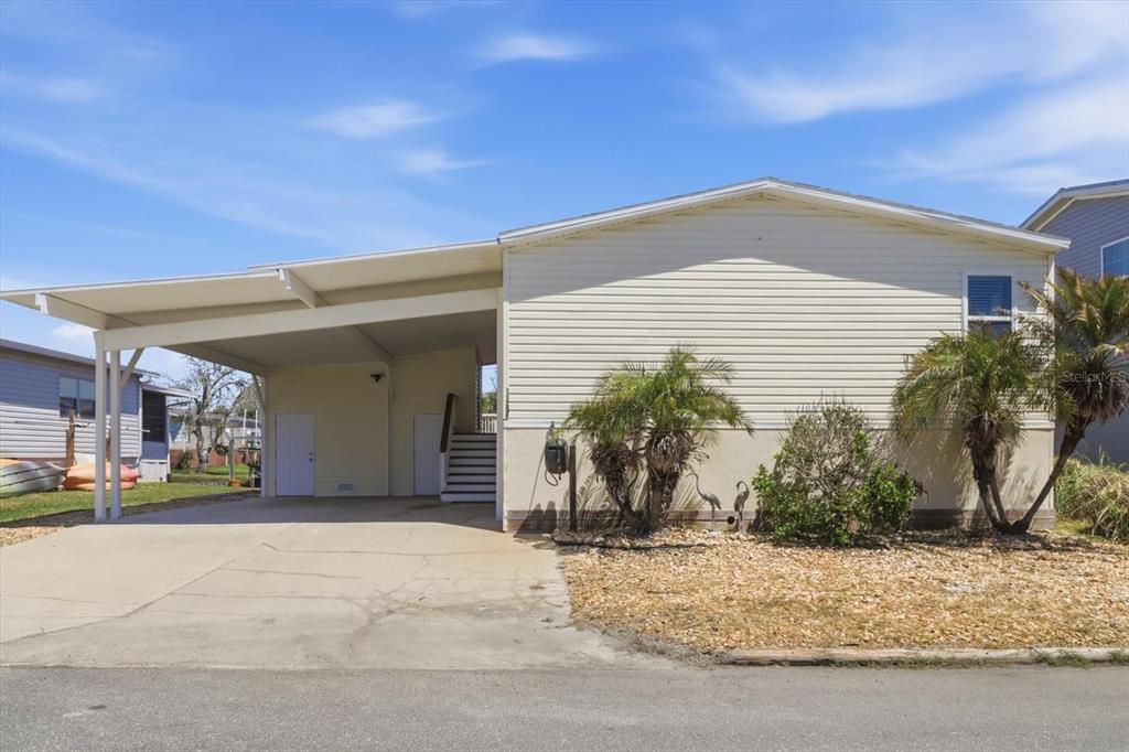 A light-colored manufactured home features a large attached carport and a gravel front yard — 11673 W CLEARWATER COURT, HOMOSASSA, FL