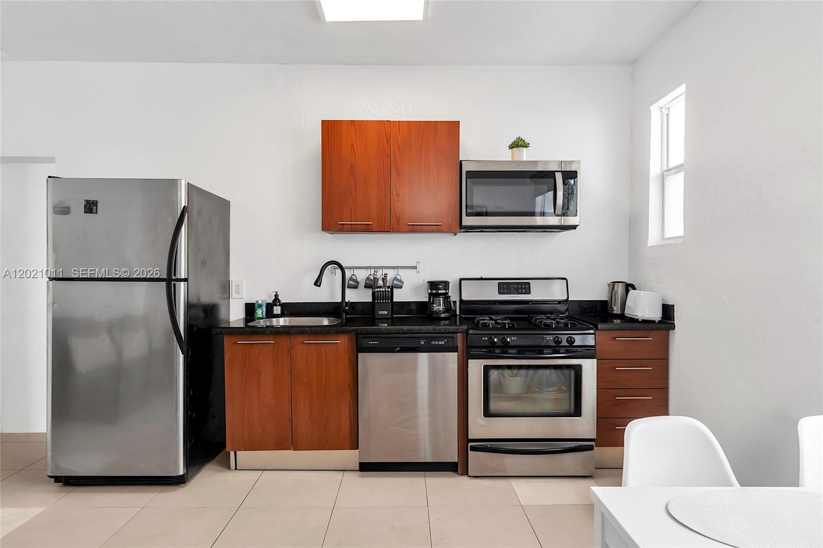 A kitchen features stainless steel appliances, wood cabinets, and black countertops against white walls — 500 14th St # 101, Miami Beach FL 33139, MIAMI BEACH, FL