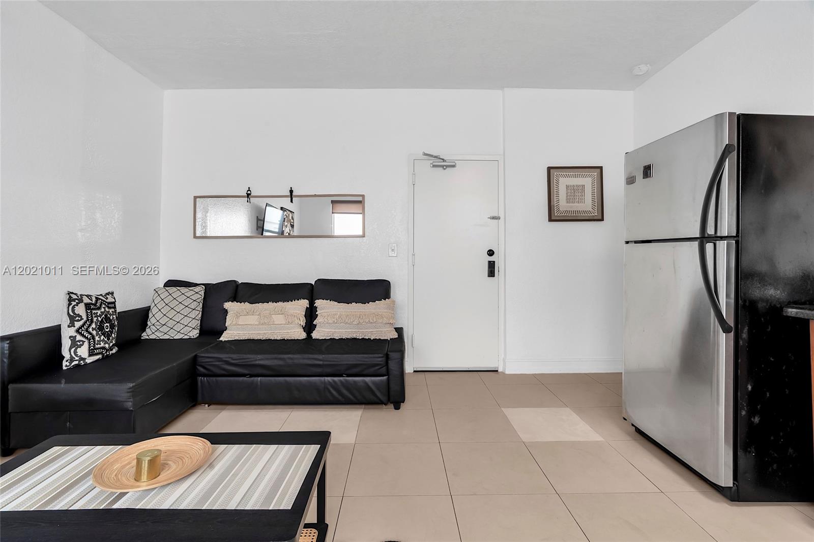 A living room features a black sectional sofa, a coffee table, and a stainless steel refrigerator — 500 14th St # 101, Miami Beach FL 33139, MIAMI BEACH, FL